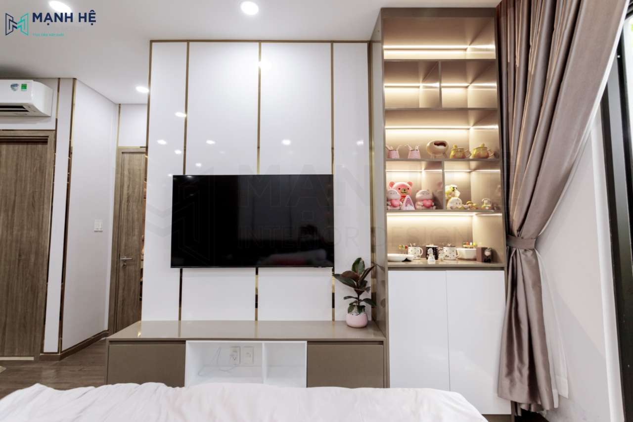 Điểm nhấn đến từ kệ tivi kế hợp tủ trang trí bên hông. Decor thêm các món trang trí cho phòng ngủ thêm sinh động. Tủ quần áo cánh mở cửa kính sang trọng, kết hợp ghế đôn và thảm lót.